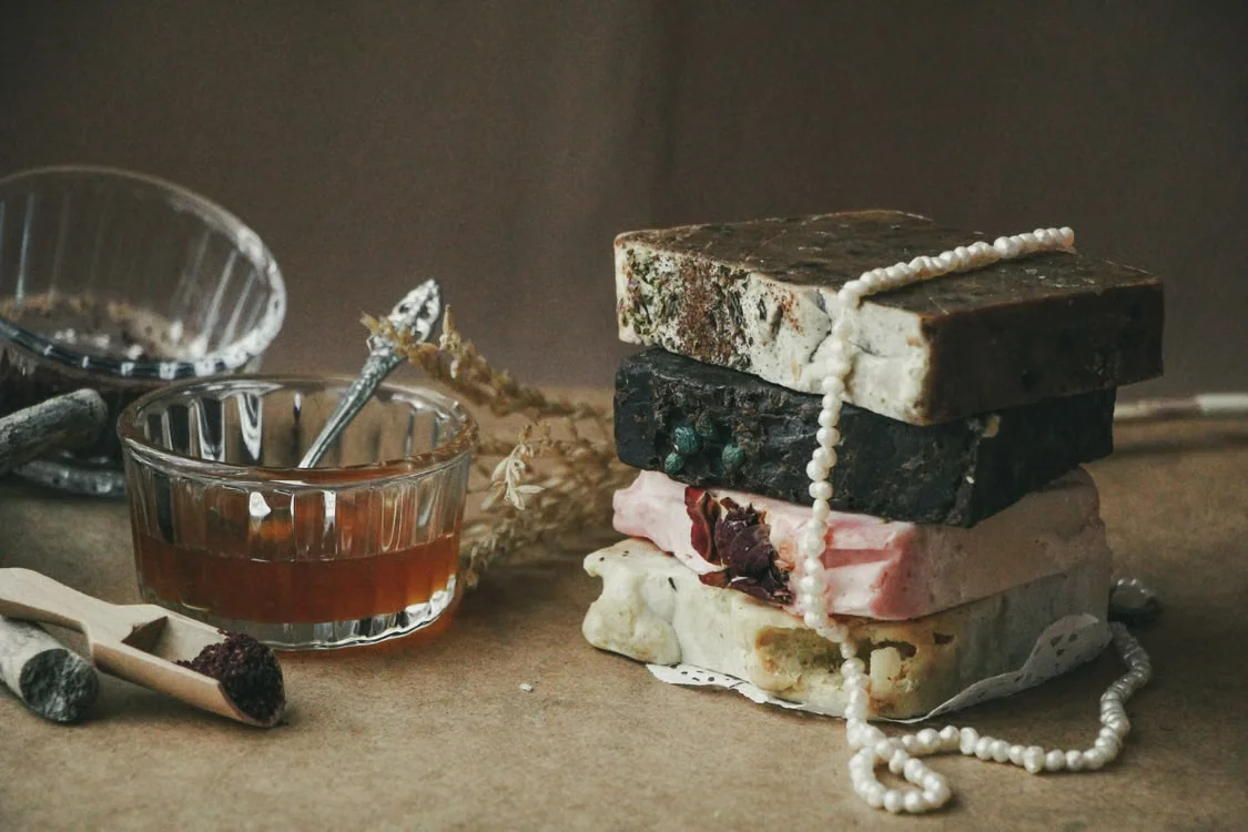 Handmade artisan soaps stacked with honey, dried botanicals, and pearls on a warm wooden surface